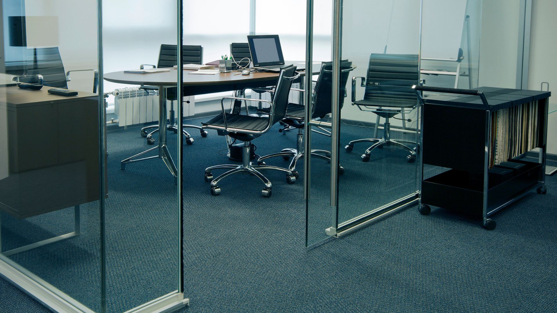 A glass walled conference room with a desk and chairs